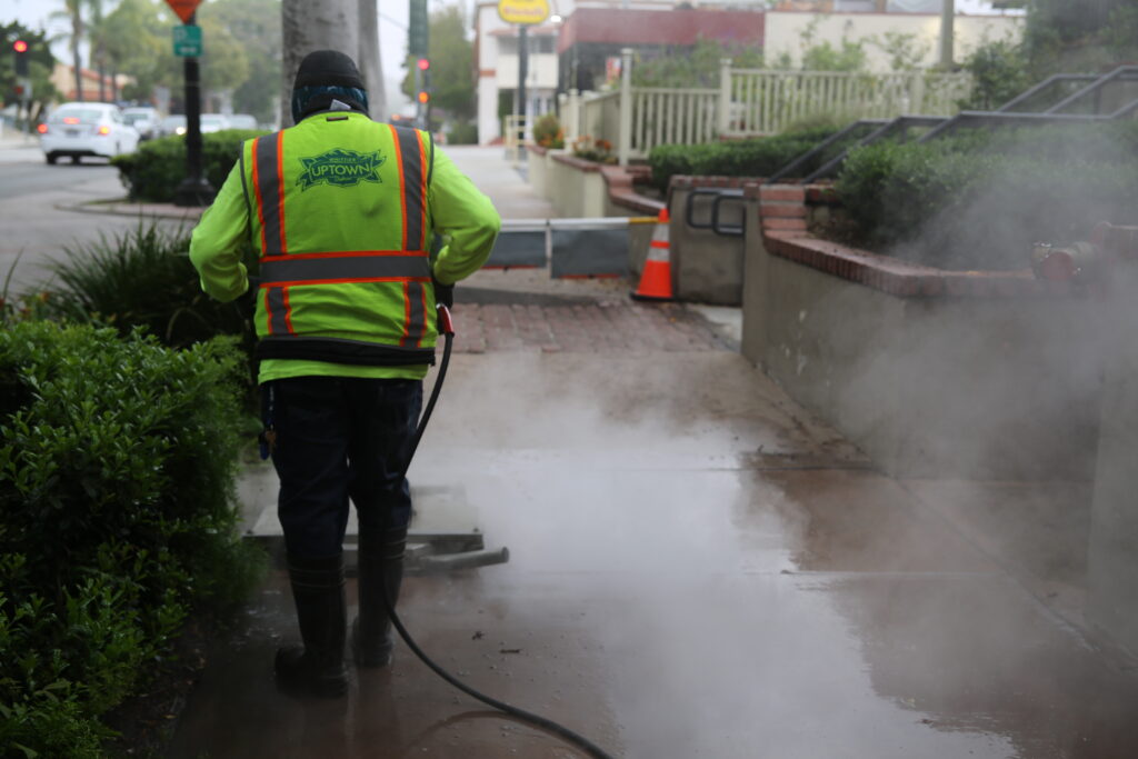 Maintenance vendor using a power washer to clean the sidewalk in Uptown Whittier